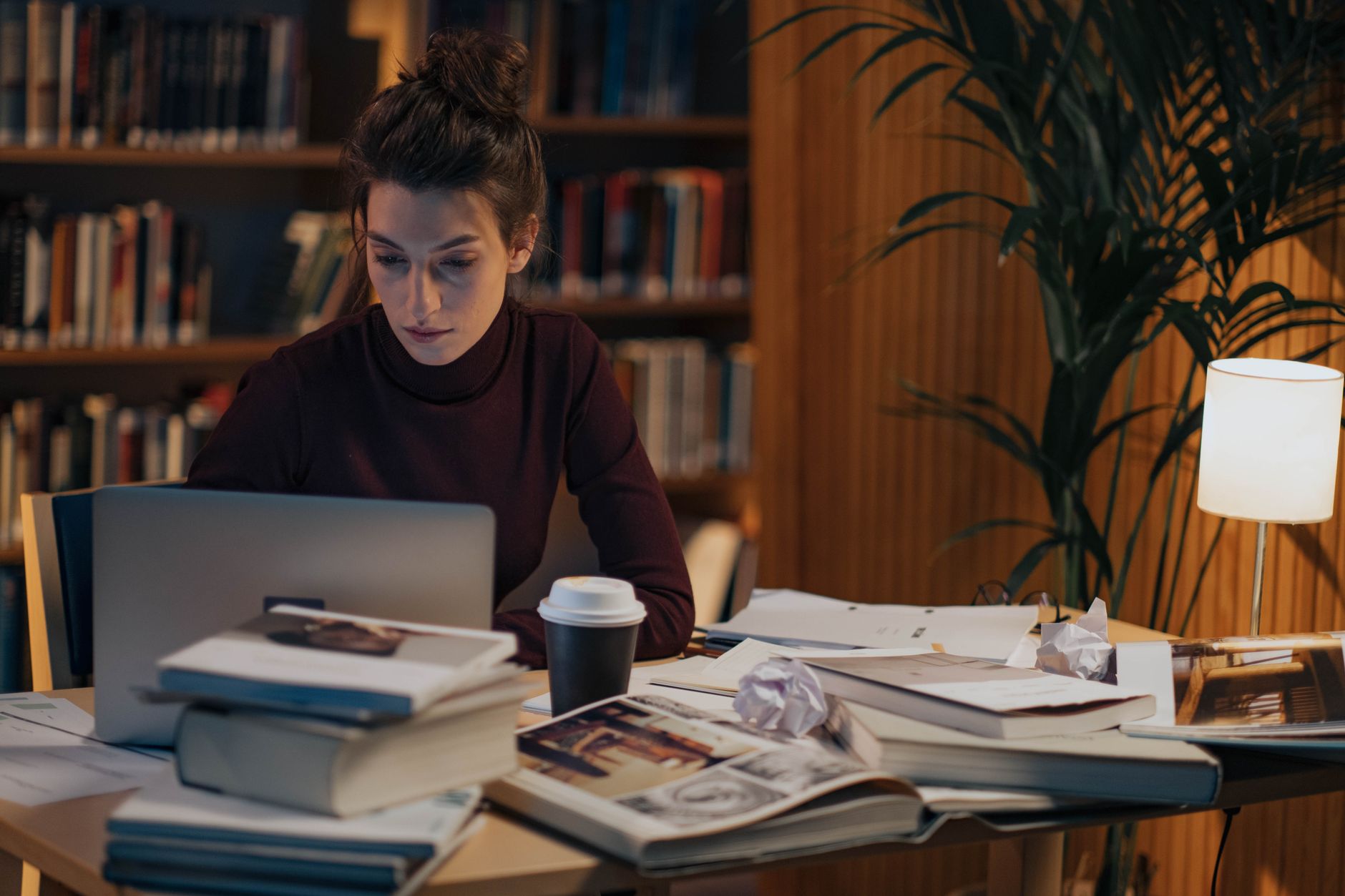 Gece geç saatlerde laptop ve kitap yığınları arasında tez yazan öğrenci